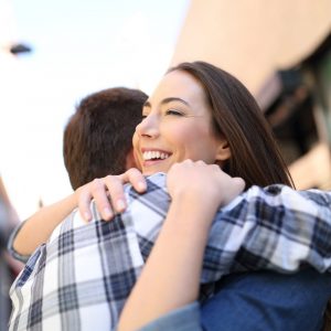 smiling, pretty brunette woman hugs man in an outdoor town setting
